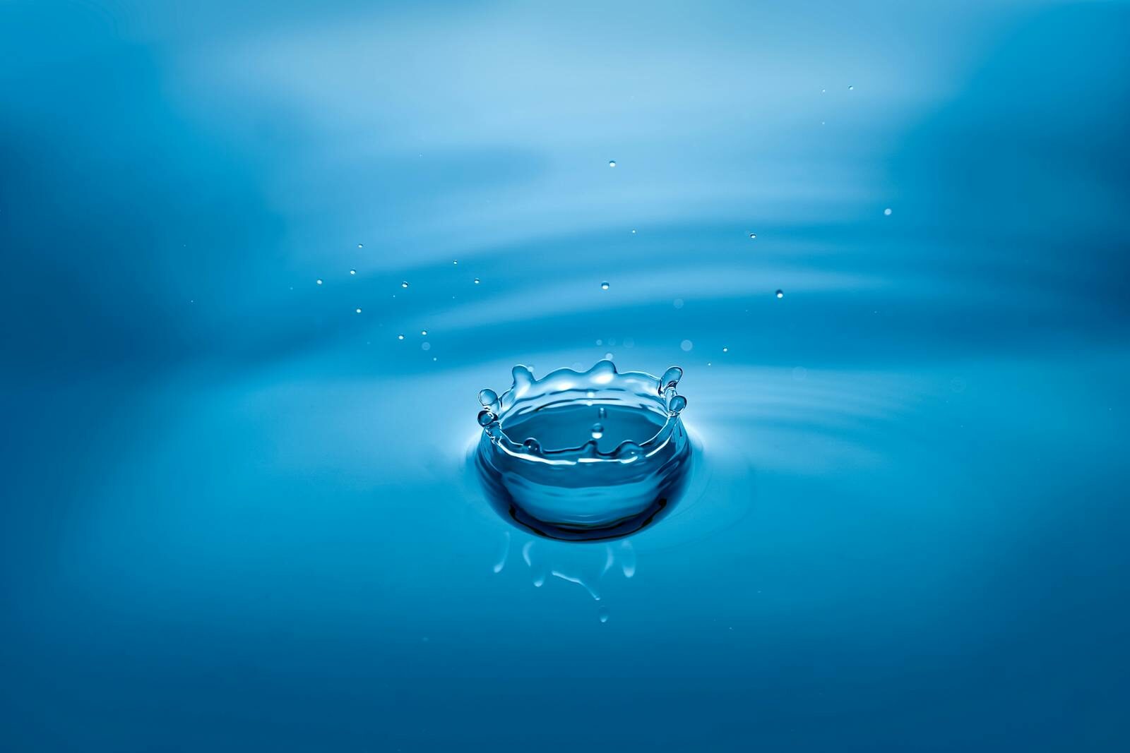 High-speed photo of a blue water droplet creating ripples and splash effects.