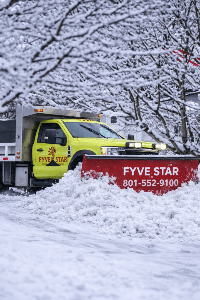 Bright yellow snow plow with a red blade clears freshly fallen snow from a residential street, promoting winter services by Fyve Star.