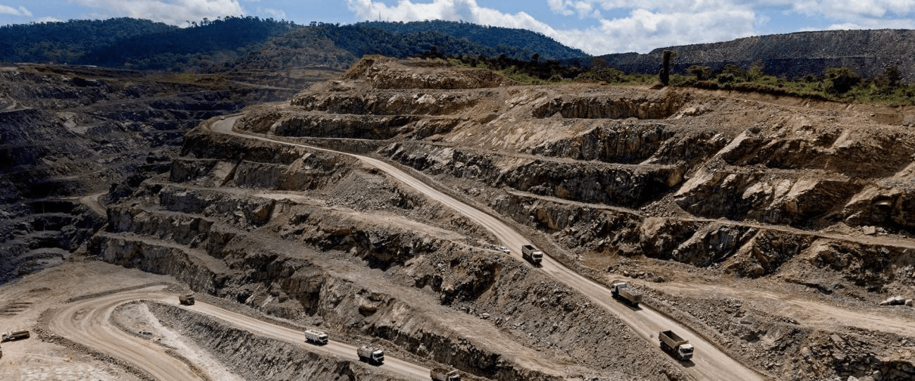 Open-pit mining site with trucks traversing winding roads through layered rock formations; illustrates industrial extraction processes and landscape alteration.