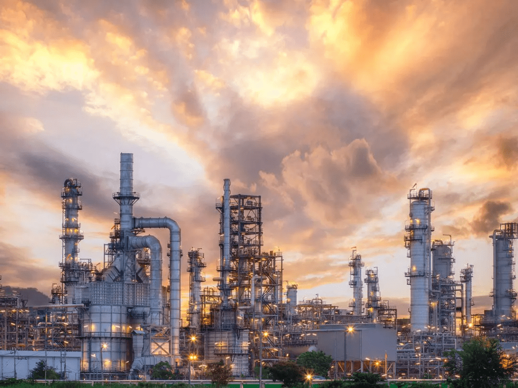 Industrial plant with rising smoke stacks and illuminated structures against a dramatic sunset sky, highlighting energy production infrastructure.