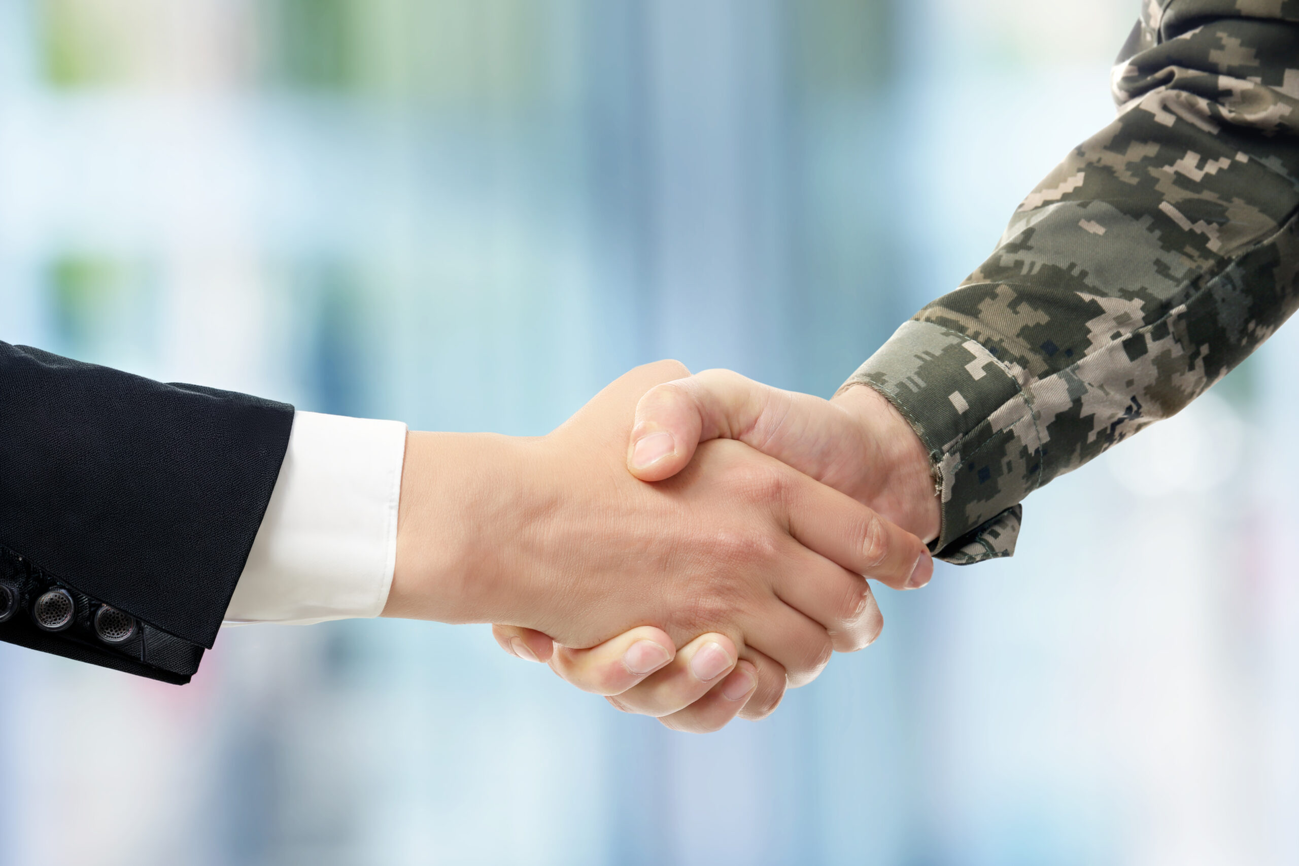 A businessperson shakes hands with a soldier, symbolizing cooperation and partnership between civilian and military sectors.