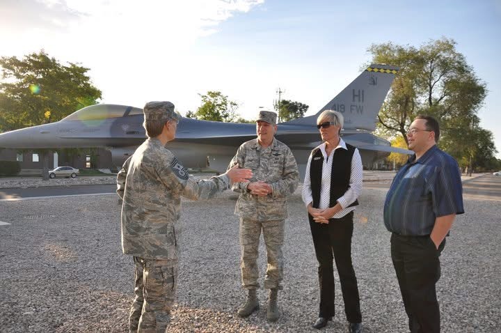 Military personnel engage in discussion near an F-16 fighter jet, highlighting collaboration and support within an Air Force base setting.