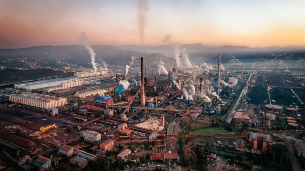 Aerial view of a factory with chimneys emitting smoke during sunset, highlighting industrial pollution