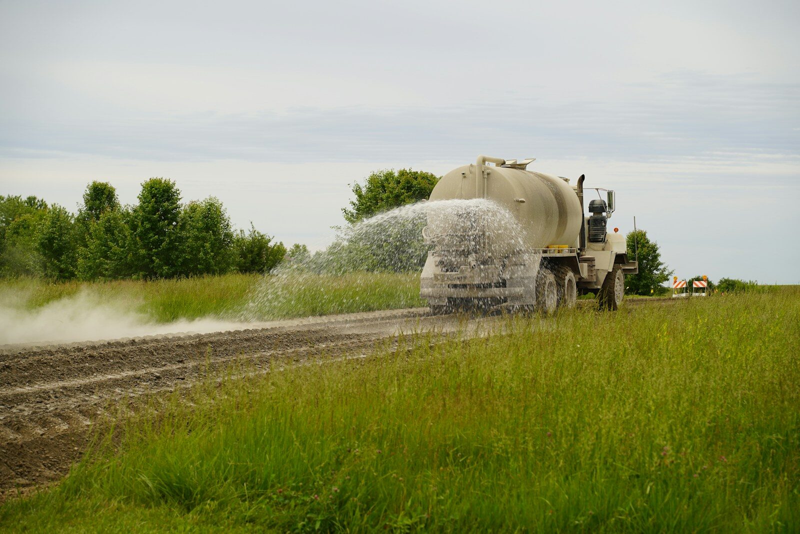 Large truck spraying water on a dusty rural road.
